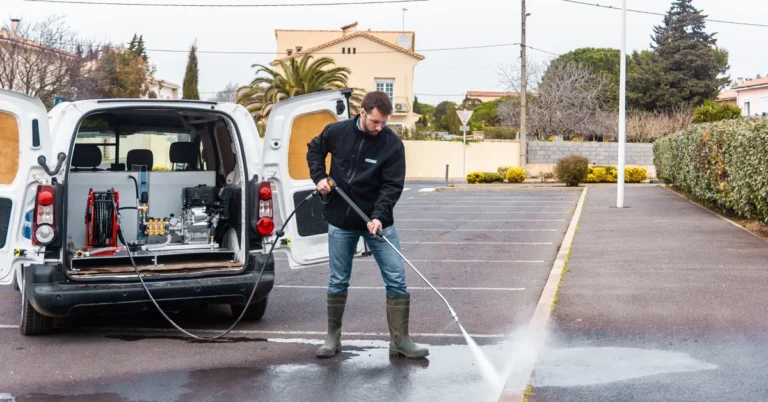 Opérateur utilisant un nettoyeur haute pression embarqué dans un utilitaire équipé d’un skid Mirage pour le nettoyage d’un parking urbain.